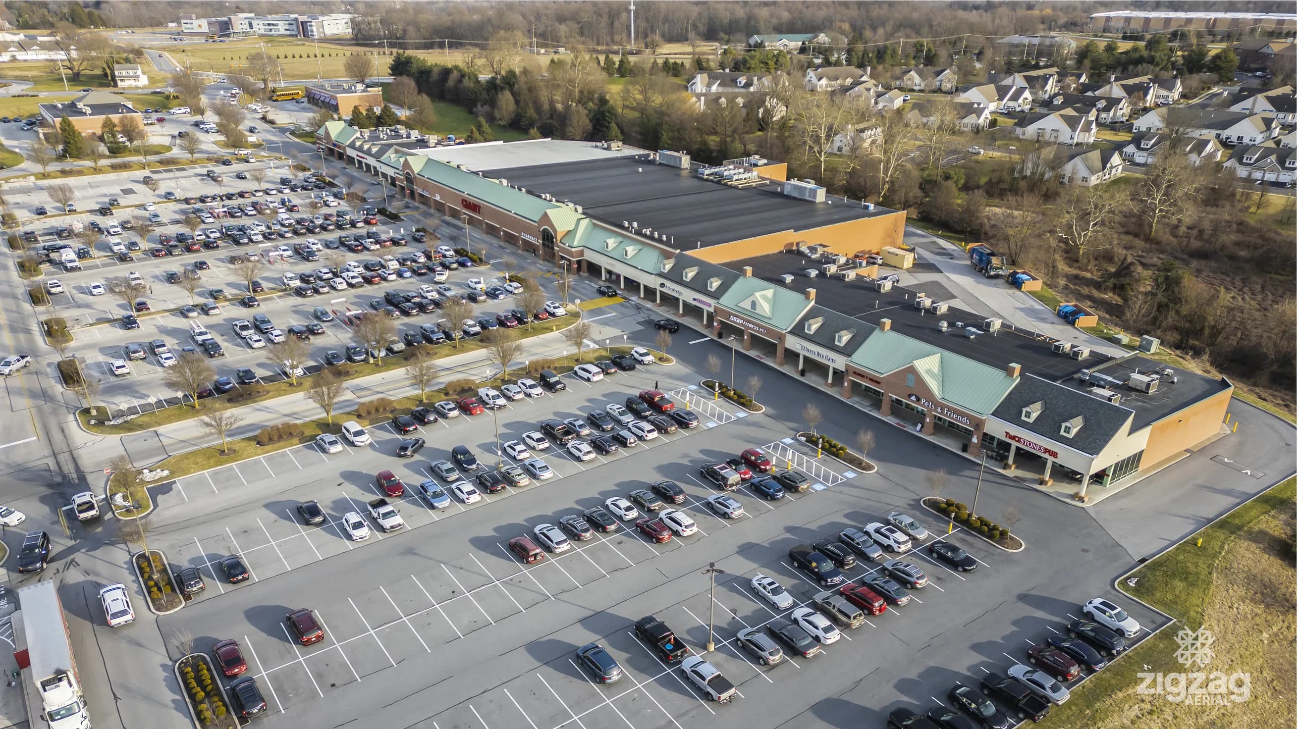 Aerial view of a retail center in Jennersville, Pennsylvania, showing the anchor store, its row of storefronts and the full parking lot, with housing and open ground behind
