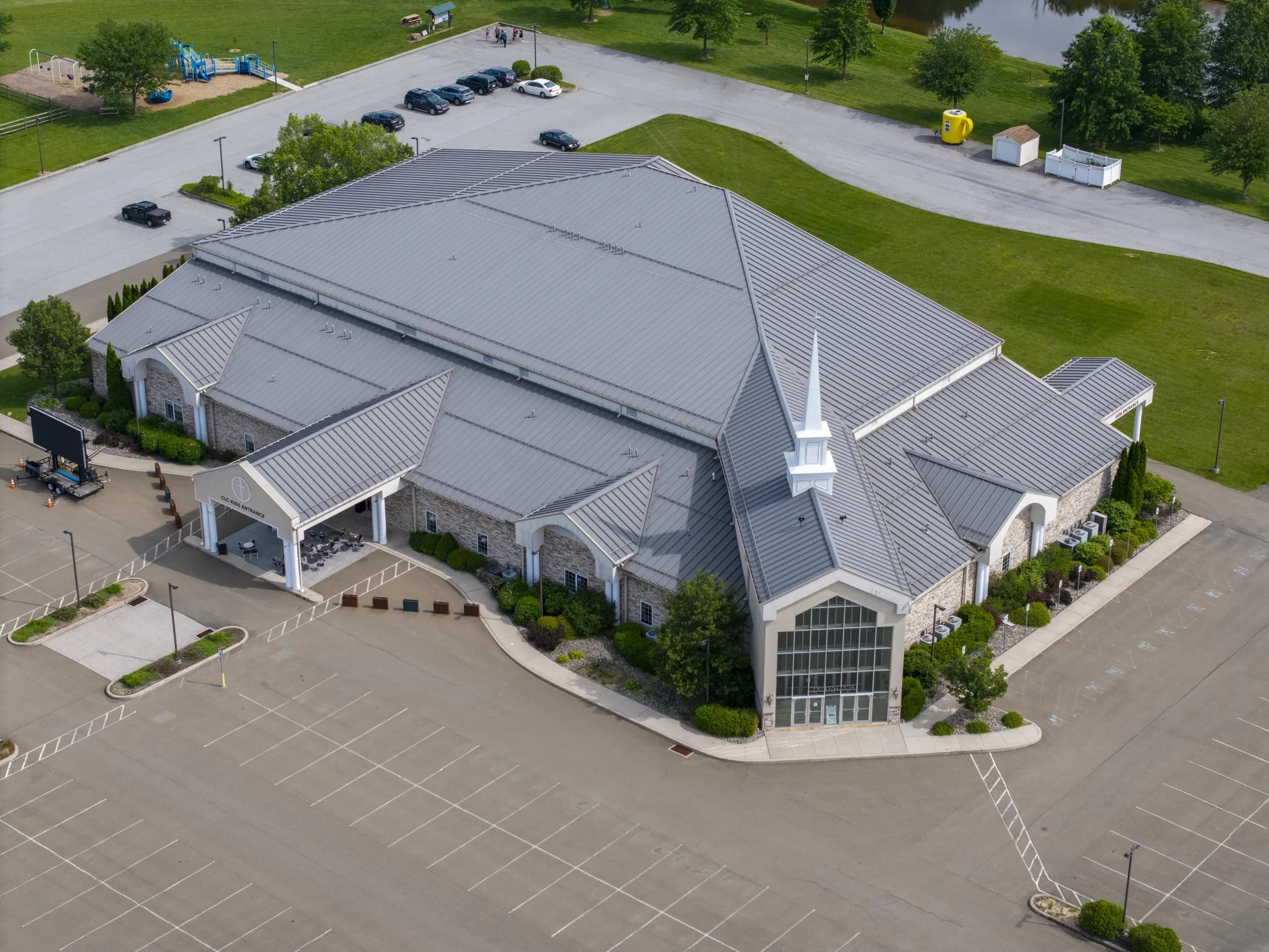 Aerial view of the Christian Life Center, a large church building with a standing-seam metal roof and white steeple, its stone entrances and surrounding parking