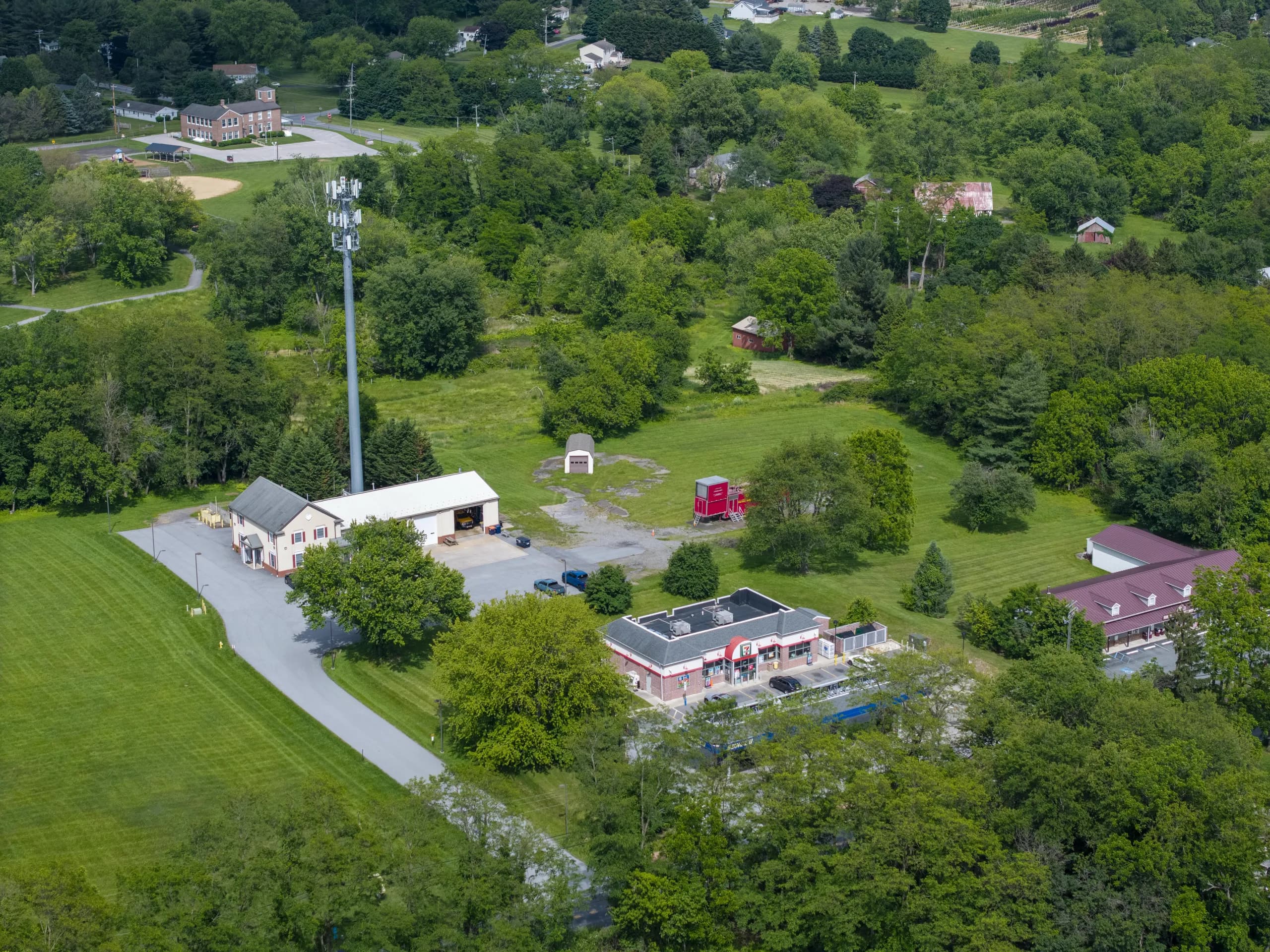 Aerial view of the village center of New London, Pennsylvania, with the fire company building, a convenience store and fuel canopy, a cell tower, and the school grounds and farmland beyond