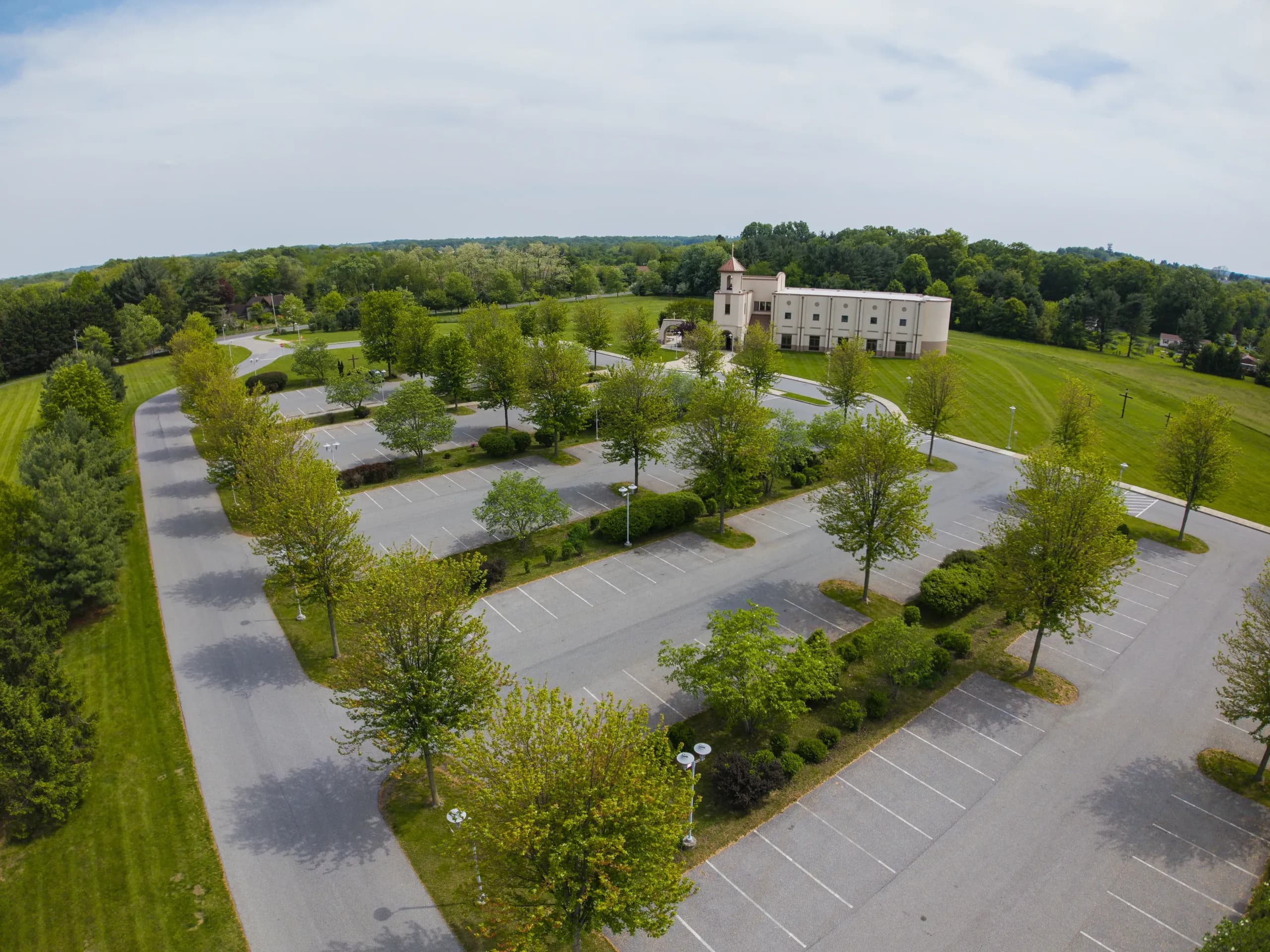 Aerial view of St. Rocco church in Avondale, Pennsylvania, the building set behind a tree-lined parking lot with lawns and woodland around it