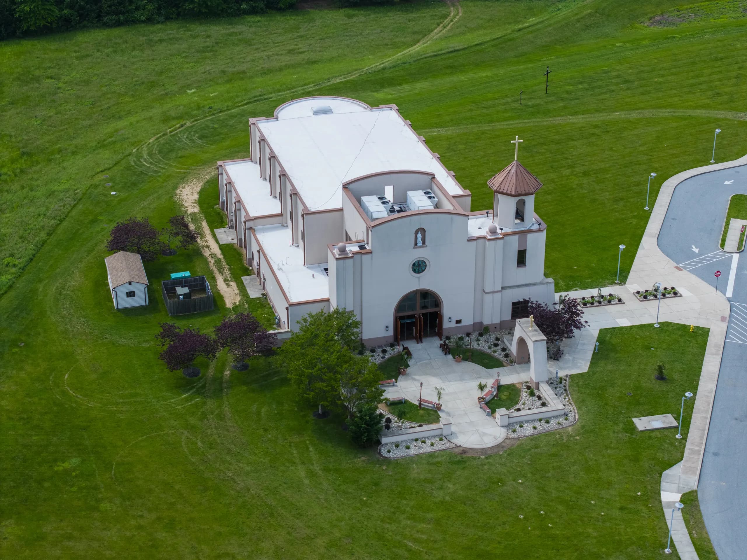 Overhead view of St. Rocco church in Avondale, Pennsylvania, showing its flat roof and rooftop mechanical units, the bell tower and cross, and the landscaped forecourt at the entrance